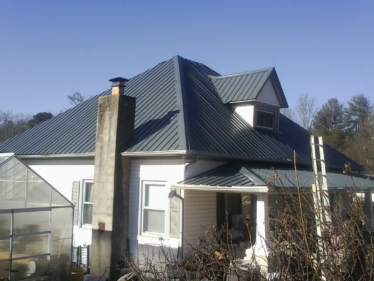 Dark blue standing seam metal roof on a white farmhouse with dormer — Slate & Tile Roof Repair by Roofing Brothers in Allons