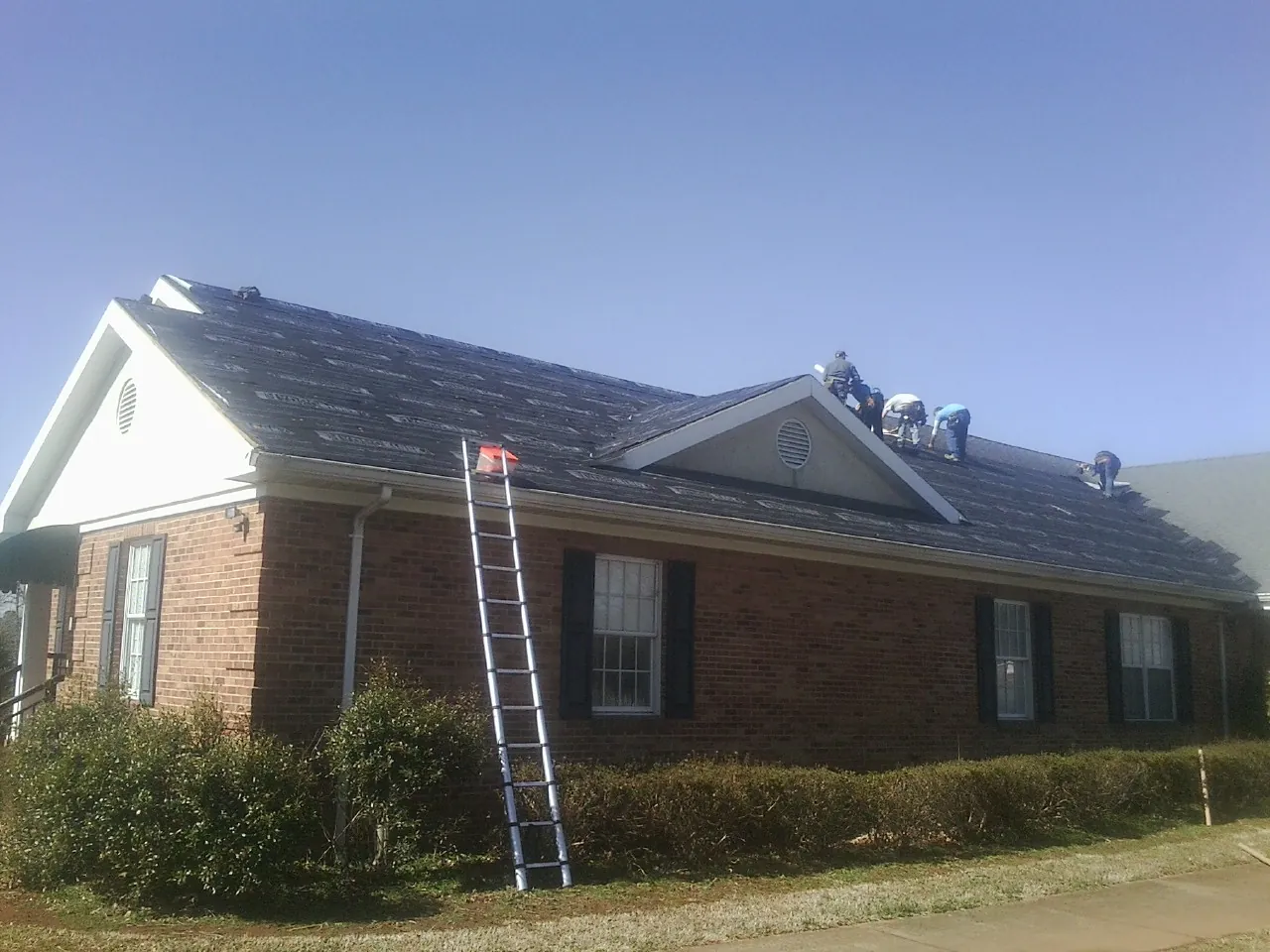 Crew tearing shingles off a brick ranch roof with a ladder set — Emergency Roof Repair work by our crew in Allons