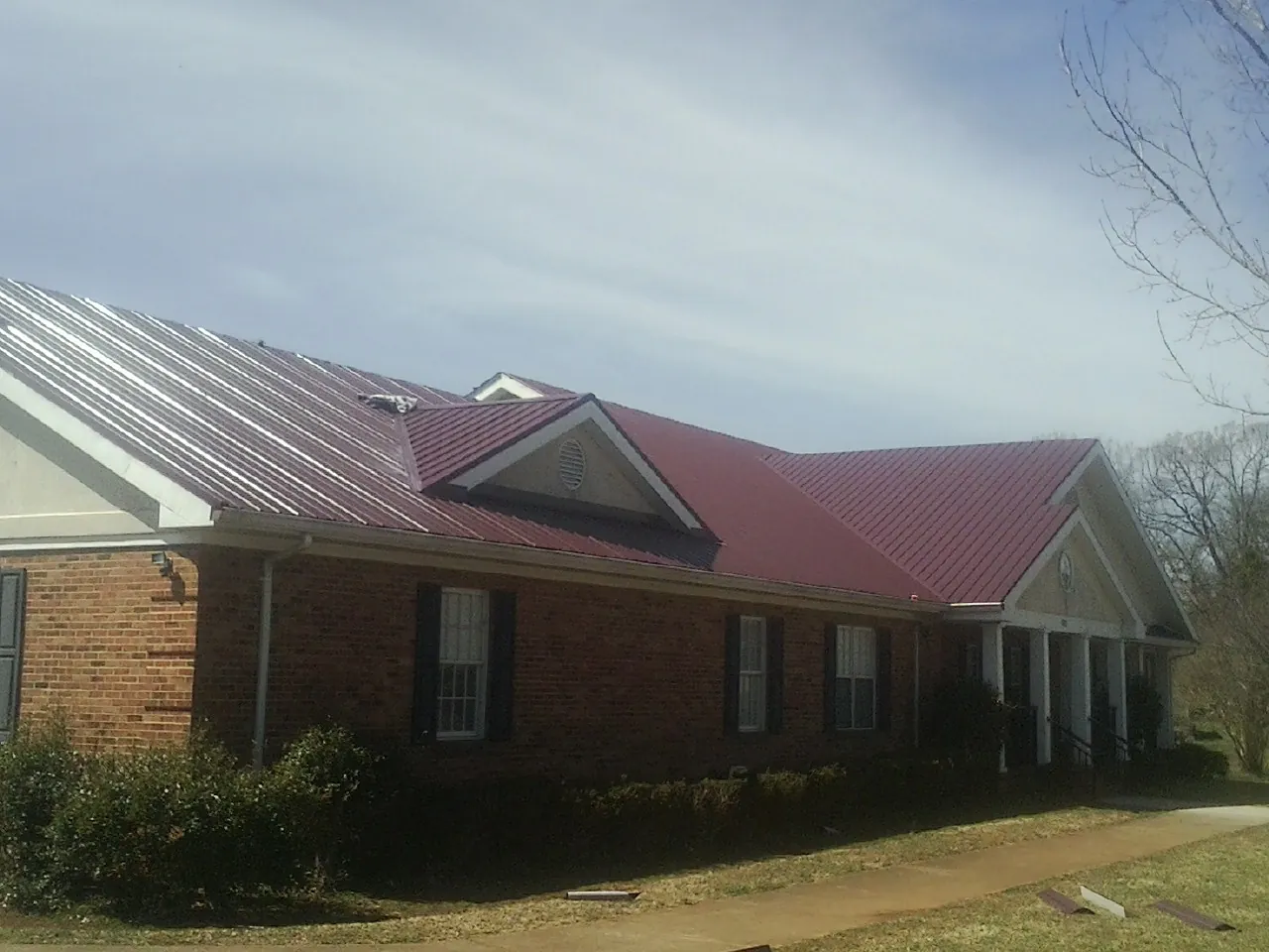 Red metal roof with gabled entries on a long brick building, from a Hail Damage Roof Repair job in Allons