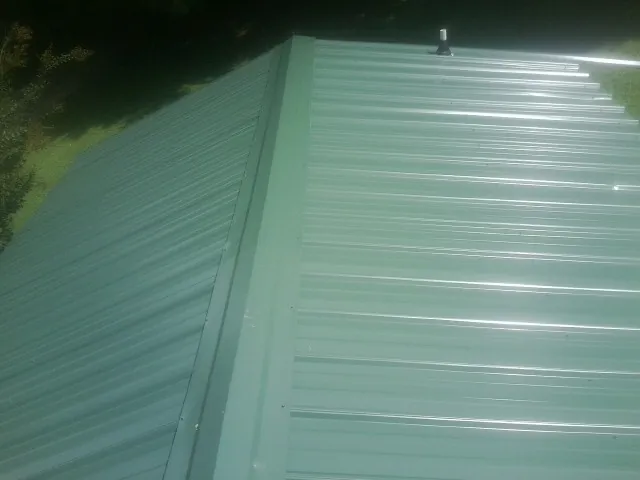 New green metal panels meeting at the ridge of a roof — Flat Roof Repair work by our crew in Allons