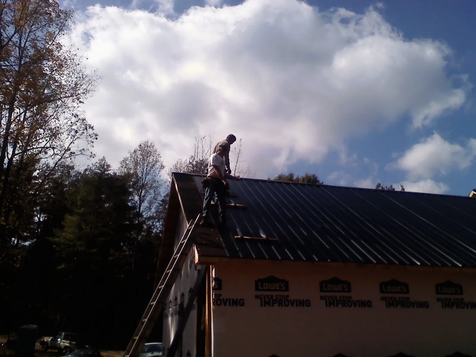 Roofer fastening dark metal panels high against a cloudy sky, from a Roof Inspection job in Allons