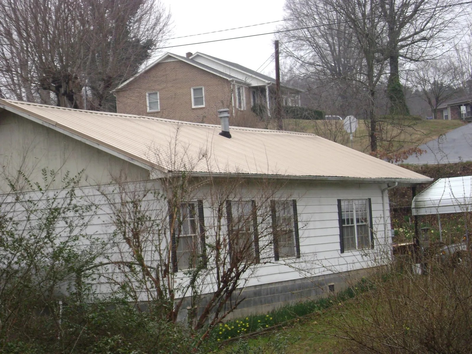 Tan metal roof on a white sided house set into a hillside — Commercial Roofing by Roofing Brothers in Allons