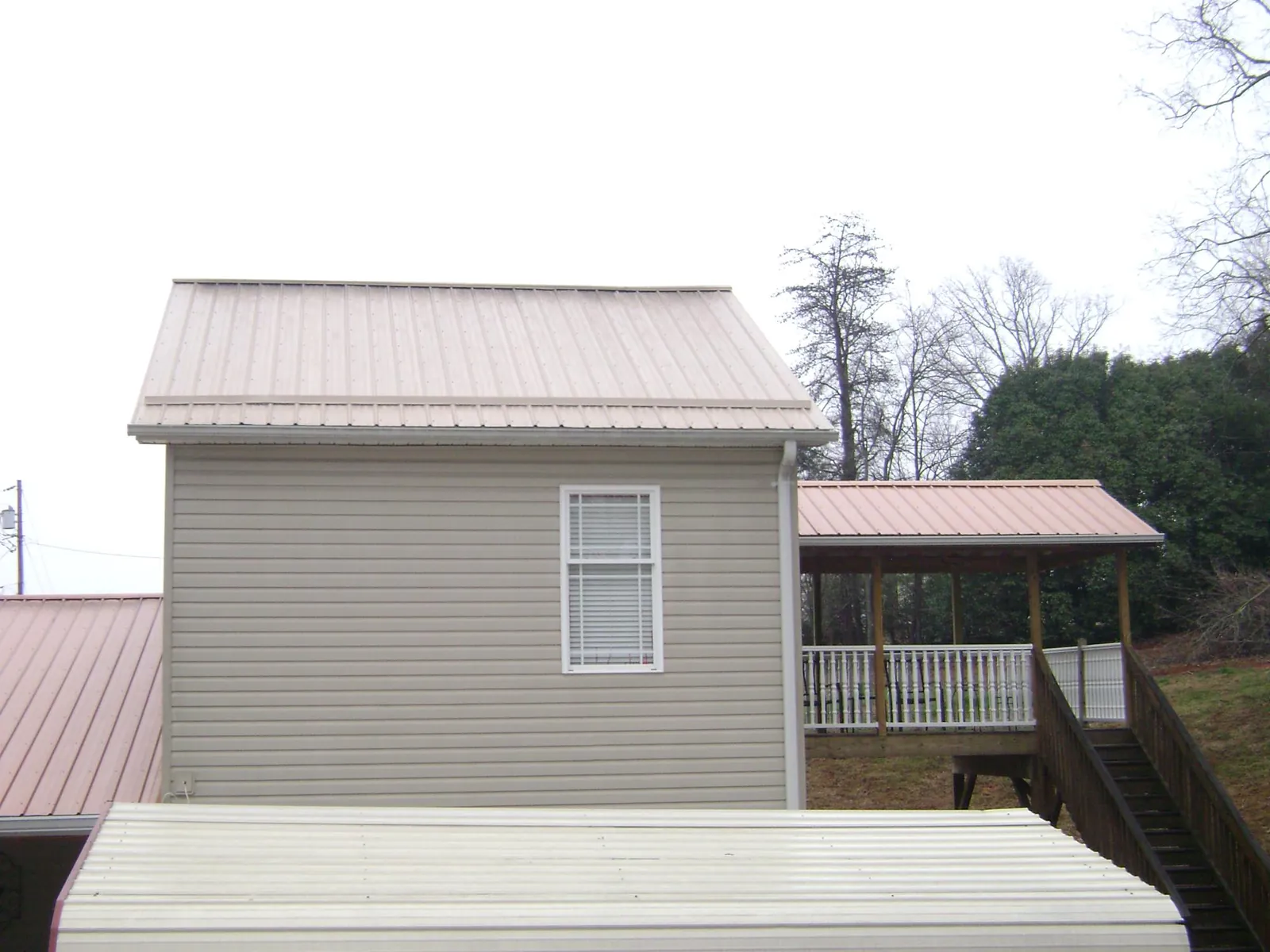 Tan metal roofs on a two story addition and attached porch, from a Roof Replacement job in Allons